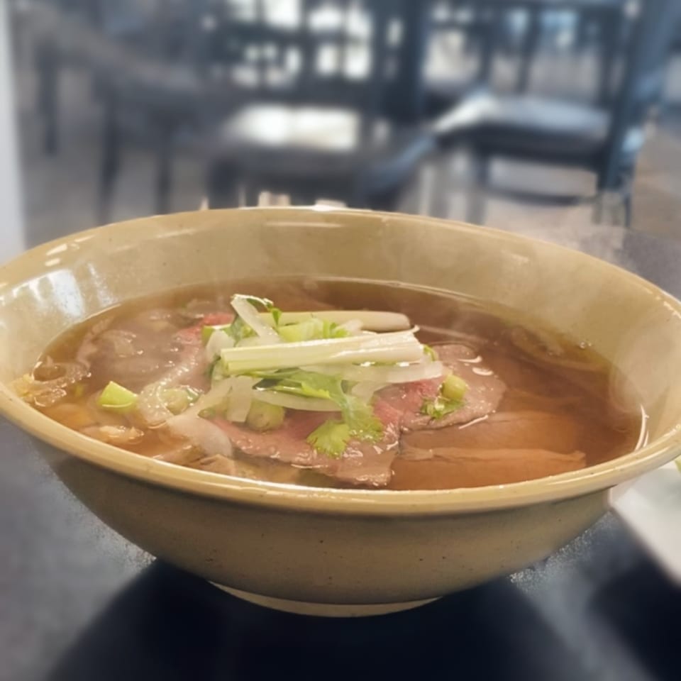 Steaming bowl of Pho Binh's Vietnamese pho with beef, green onions, and cilantro.
