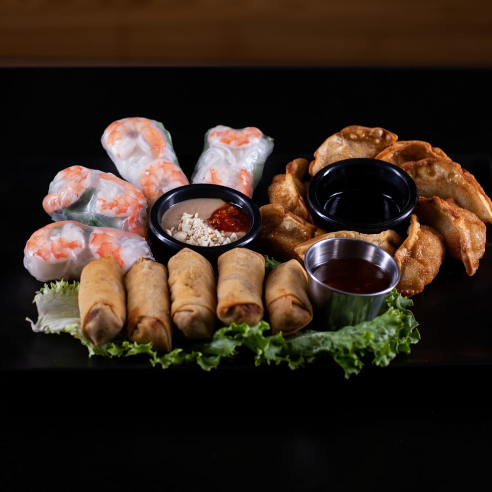 A platter of Vietnamese spring rolls, fried dumplings, and egg rolls with dipping sauces on lettuce.