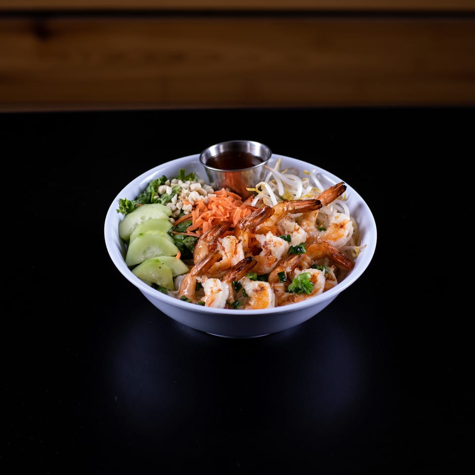 A vibrant Vietnamese shrimp noodle bowl with fresh vegetables, peanuts, and a side of sauce.