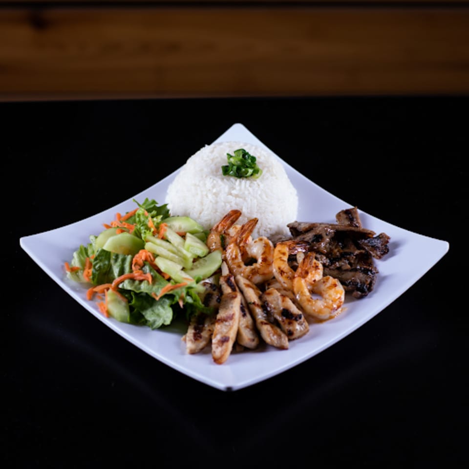 Vietnamese grilled shrimp, chicken, and beef with rice and a side salad on a white plate.